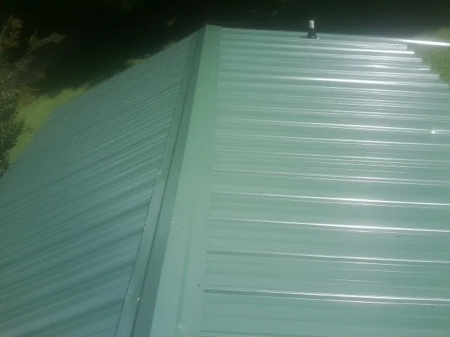 New green metal panels meeting at the ridge of a roof — Flat Roof Repair work by our crew in Lindale