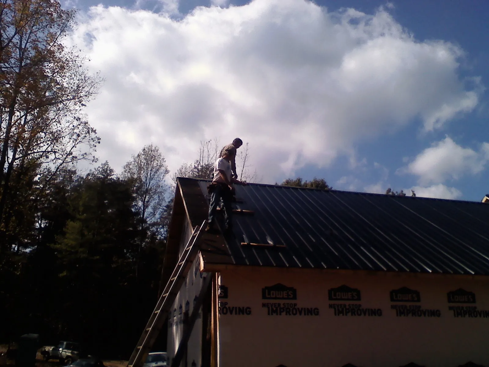 Roofer fastening dark metal panels high against a cloudy sky, from a Roof Inspection job in Lindale
