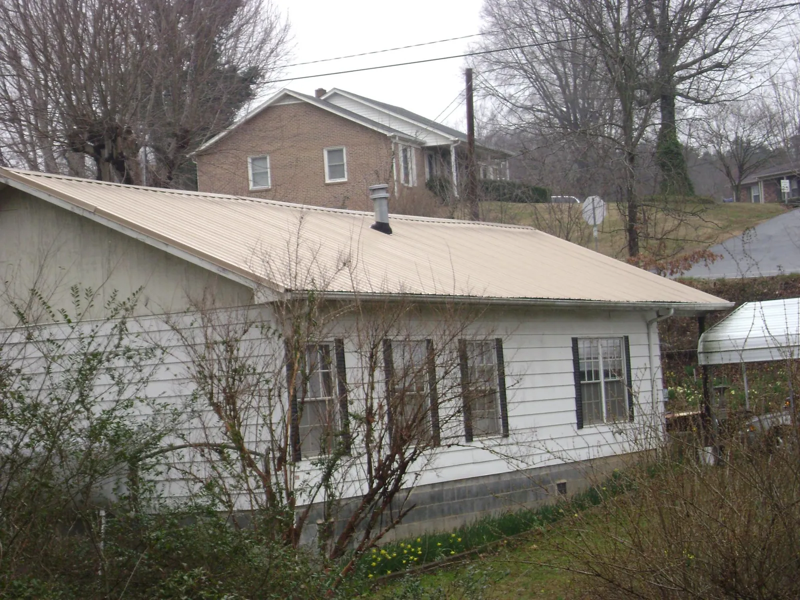 Tan metal roof on a white sided house set into a hillside — Commercial Roofing by Roofing Brothers in Lindale