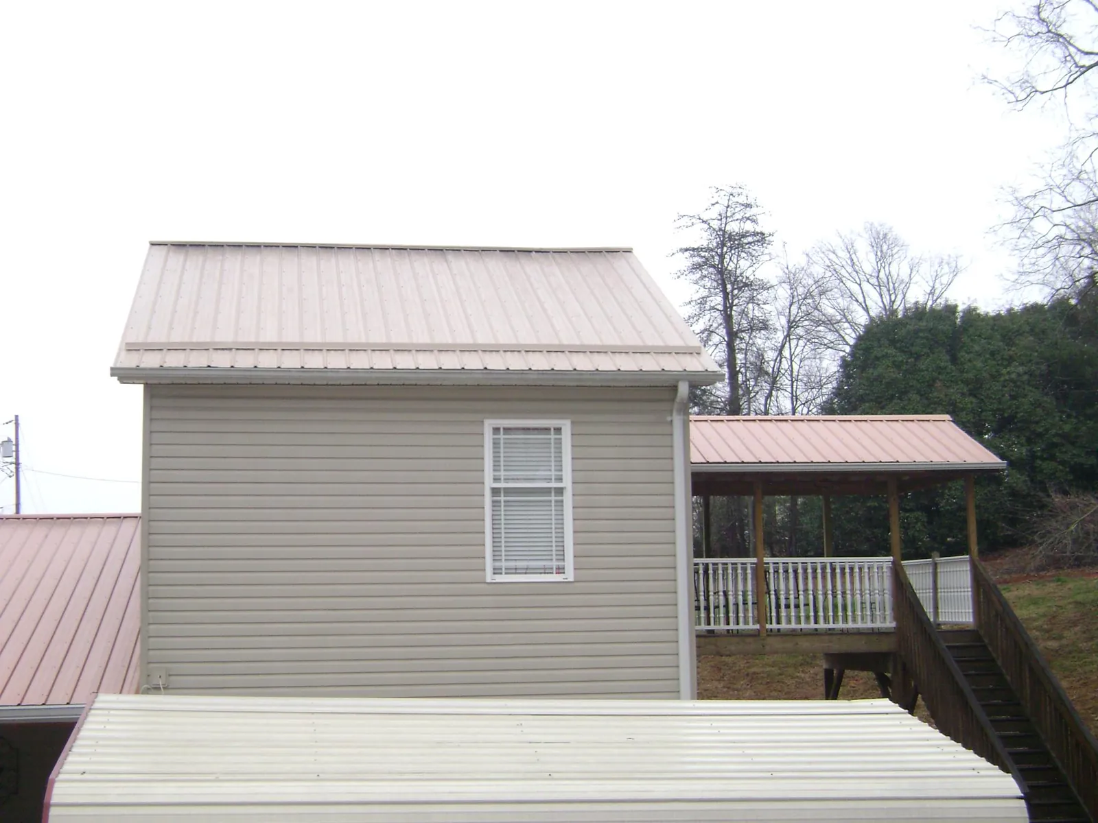 Tan metal roofs on a two story addition and attached porch, from a Roof Replacement job in Lindale